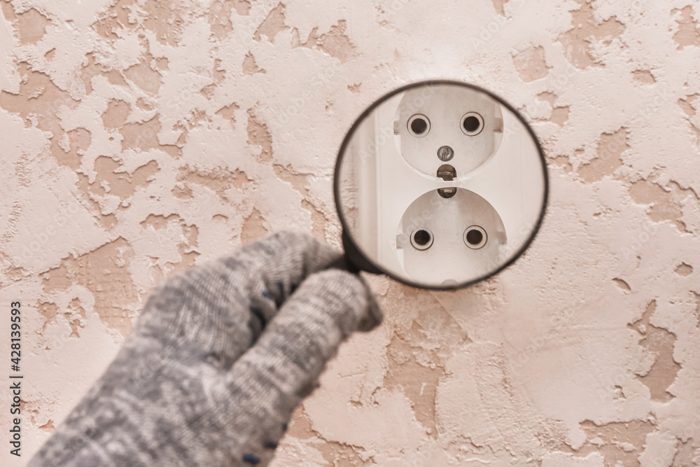 The hand of a construction worker in protective gloves examines through a magnifying glass the connection of appliances in the house The hand of a construction worker in protective gloves examines through a magnifying glass the connection of appliances in the house
