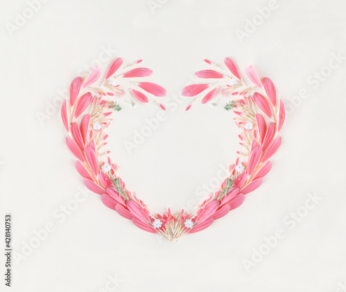 Pink color heart shaped frame made of delicate blossom petals and pale green leafs on bright beige background. Minimal flat lay. Card note love valentine concept.