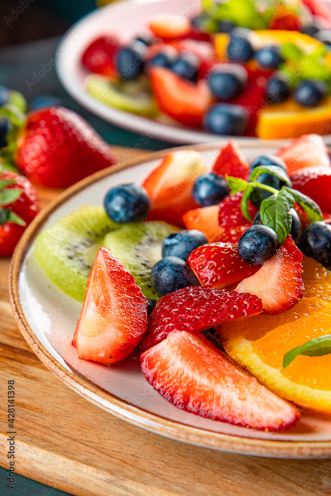 Fresh summer salad of various fruits and berries. Kiwi, orange, strawberry and blueberry on a plate decorated with mint on a table close up vertical photo soft focus Fresh summer salad of various fruits and berries. Kiwi, orange, strawberry and blueberry on a plate decorated with mint on a table close up vertical photo soft focus