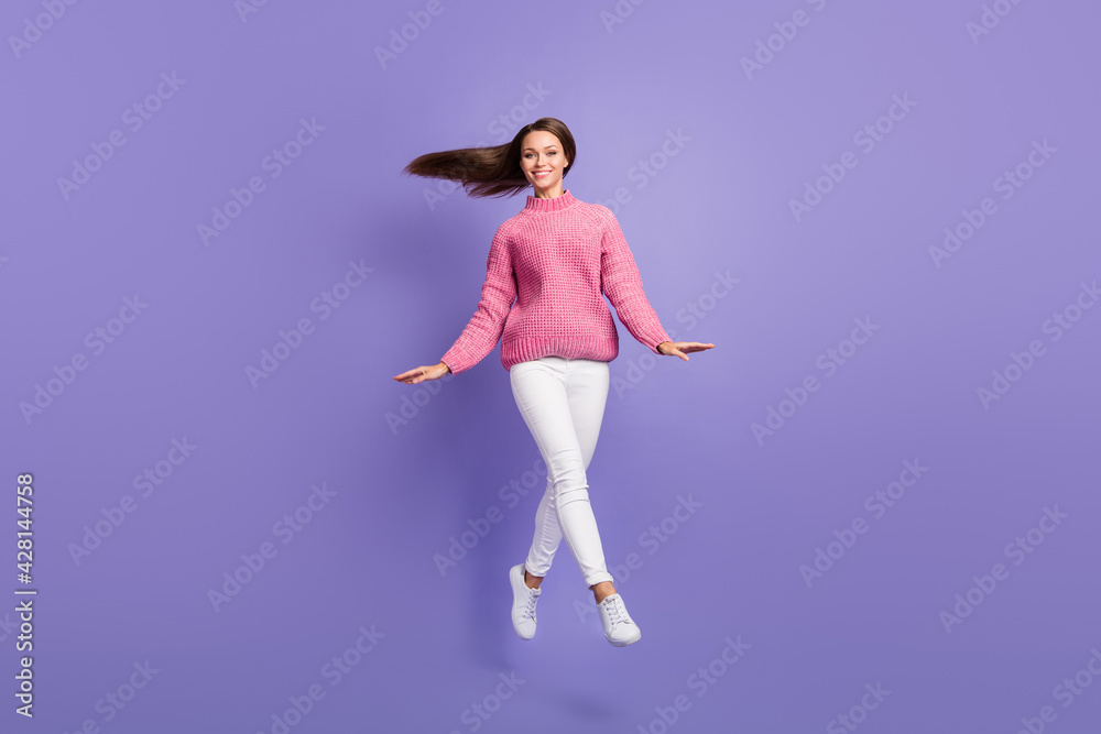 Full size photo of happy smiling cheerful young girl jumping wear pink sweater white pants isolated on violet color background