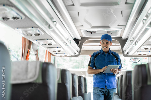 a bus crew member in uniform and a hat using a digital tablet while checking on the bus