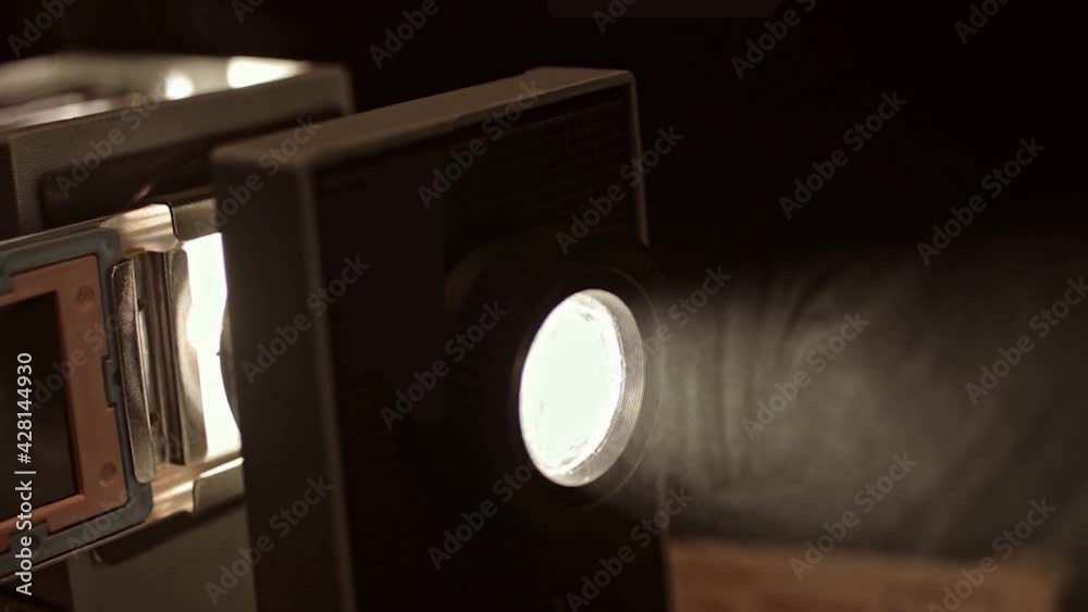 Close up of turning on retro slide projector in a dark room. Stock footage. Old fashioned vintage filmscope turned on n black background.