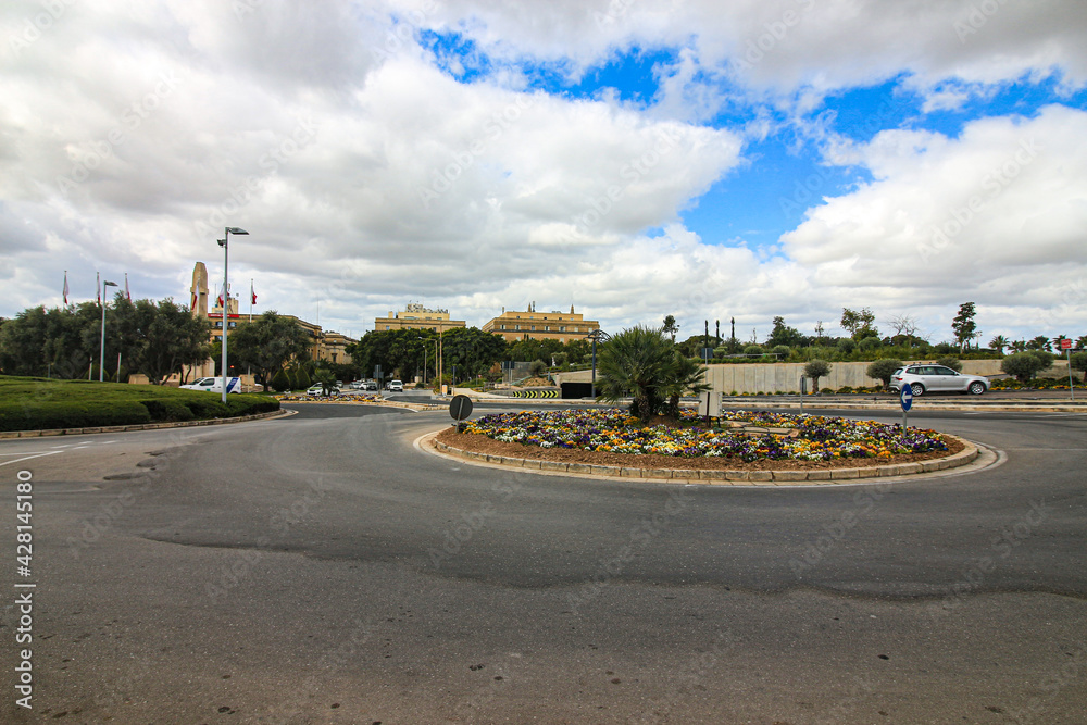 A floral covered roundabout looking towards the skyline of the town of Floriana on the Mediterranean island of Malta