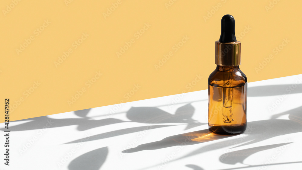 Dropper glass bottle mockup on geometric yellow and white gray concrete background with hard shadows from plants. Hard shadows. Creative cosmetic background. Banner