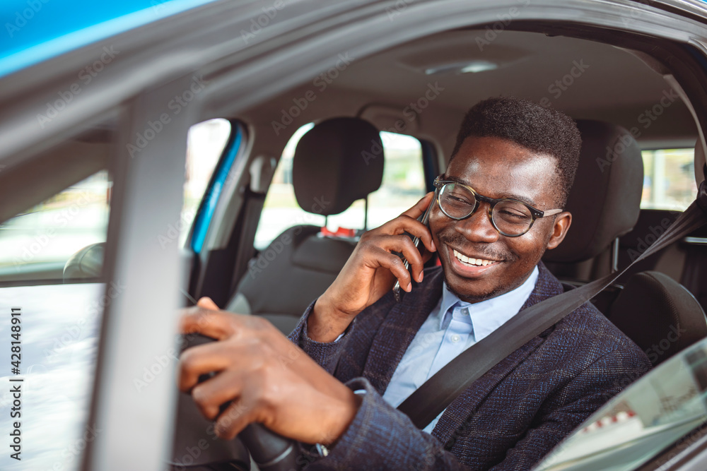 Businessman using mobile phone while driving a car. Nice business talk. Handsome young businessman talking on his smart phone and smiling while sitting on the front seat Businessman using mobile phone while driving a car. Nice business talk. Handsome young businessman talking on his smart phone and smiling while sitting on the front seat