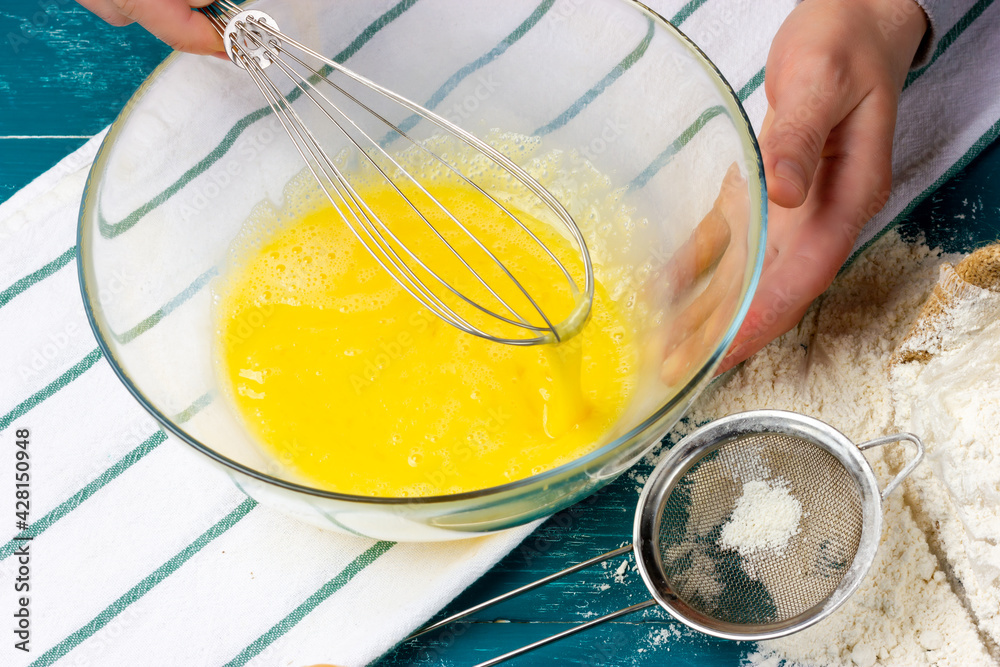 The process of beating chicken eggs with a hand whisk. Yellow dough mass in a glass bowl. The process of beating chicken eggs with a hand whisk. Yellow dough mass in a glass bowl.
