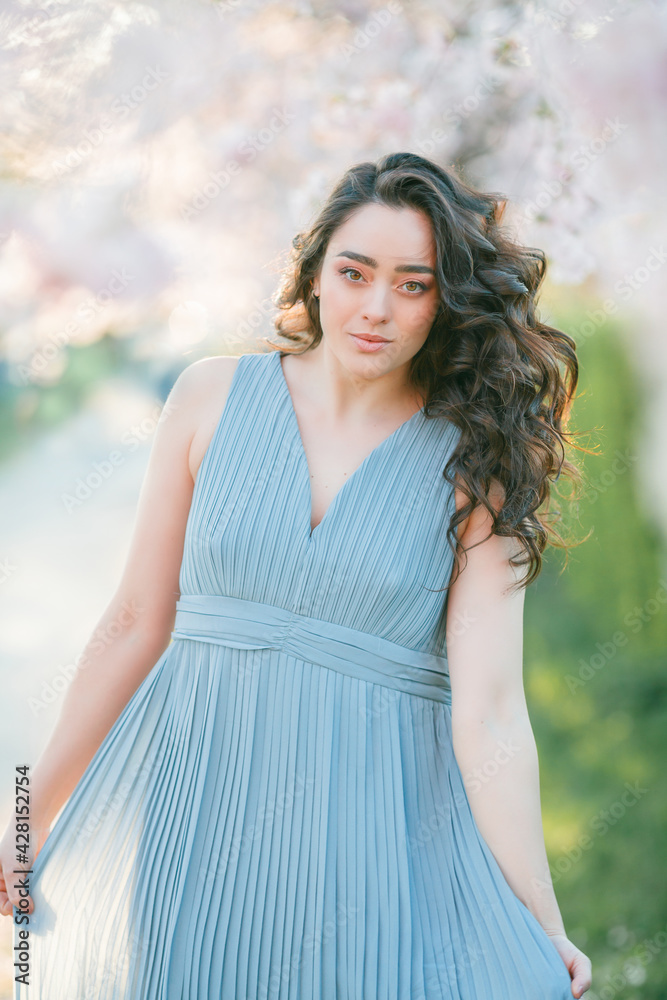 Beautiful young woman with curly hair is resting in the blooming sakura garden. Beautiful young woman with curly hair is resting in the blooming sakura garden.