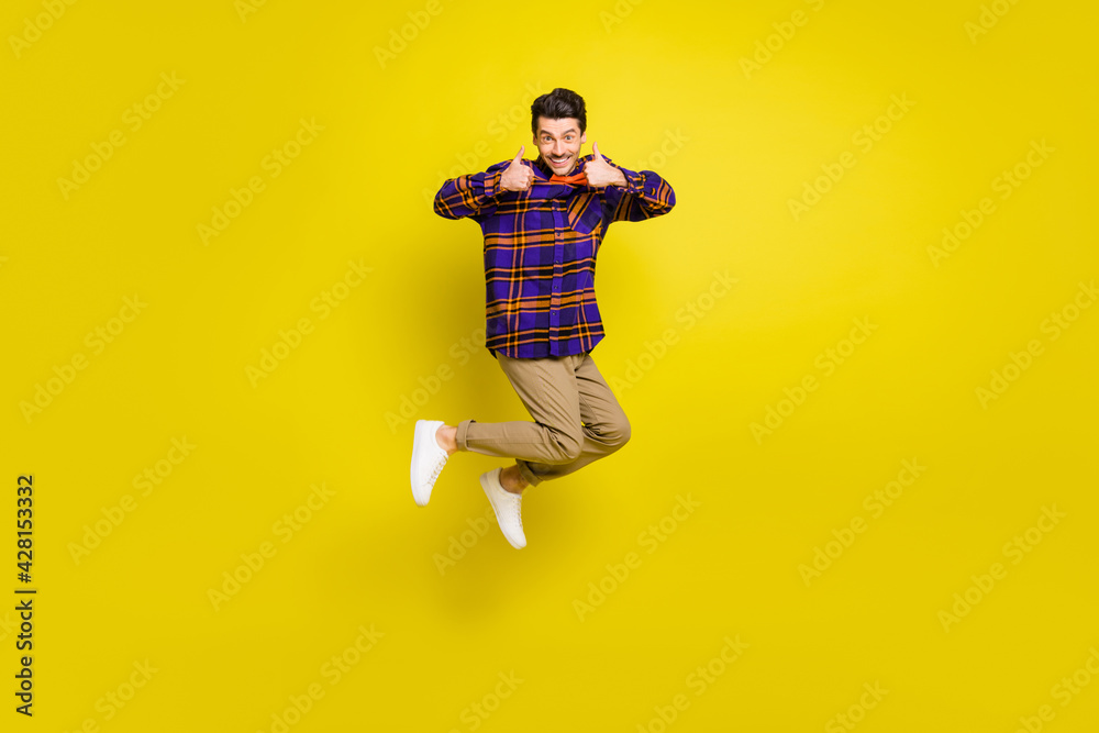 Full size photo of young excited man jump happy smile show thumb-up like cool advert advice isolated over yellow color background