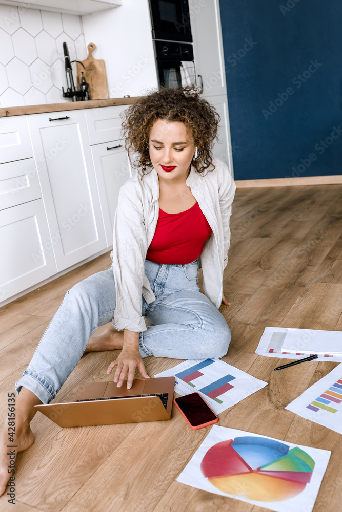 Beautiful business woman is sitting on the floor at home, using laptop, smiling. Stylish young female employee working remotely on new project, making a financial report or presentation Beautiful business woman is sitting on the floor at home, using laptop, smiling. Stylish young female employee working remotely on new project, making a financial report or presentation