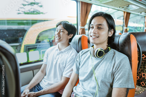 a young Asian boy and a guy with headphones sitting by the window enjoying the bus ride