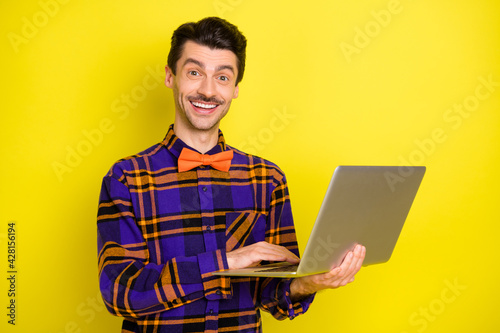 Photo of happy smiling good mood smiling lovely man working in laptop programmer isolated on yellow color background