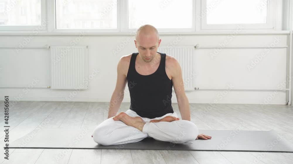 Yoga man sits on mat on floor training correct yoga breathing, handsome calm bald male engaged in yoga. Yoga man sits on mat on floor training correct yoga breathing, handsome calm bald male engaged in yoga.