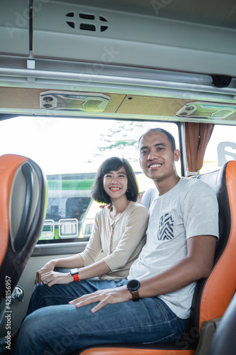 a man and a woman smile while sitting together in a bus seat while traveling