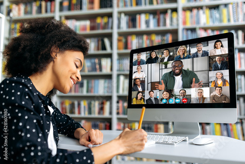 Video call, online education. African American happy female student, learning distantly, watches an online lecture, taking notes, multiracial smiling people on a computer screen, virtual communication photo