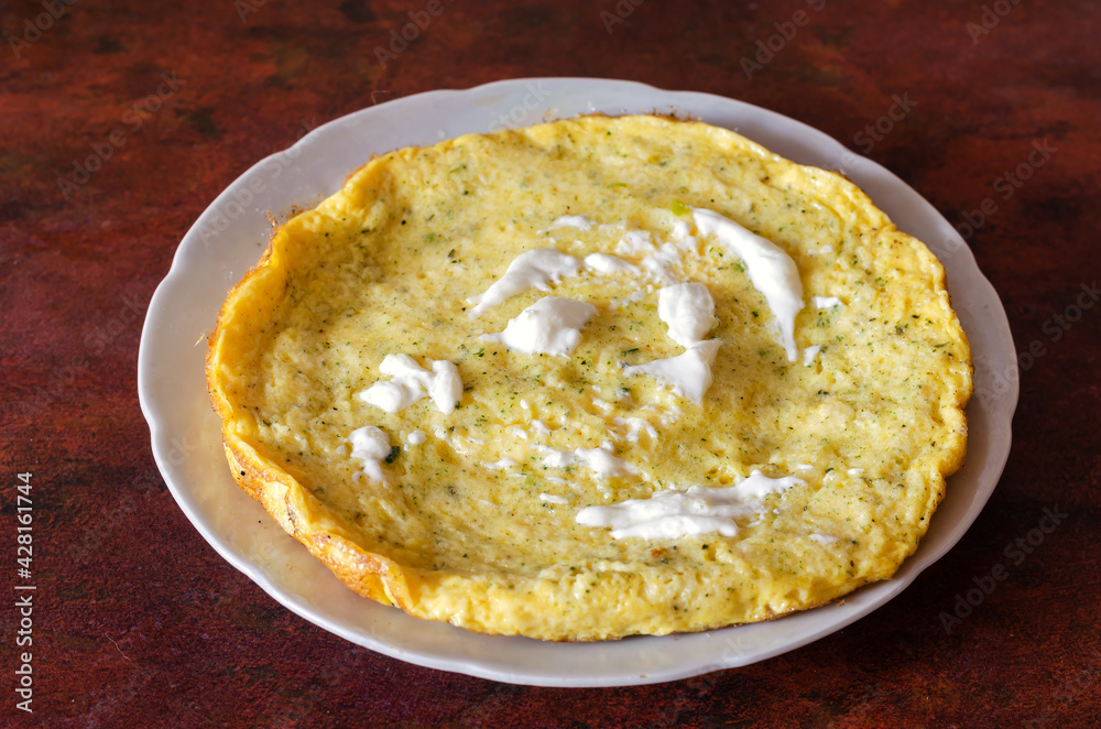 A plate with scrambled eggs, herbs and sour cream on the red kitchen table. A plate with scrambled eggs, herbs and sour cream on the red kitchen table.