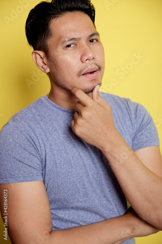 close up casual young man smile thinking idea with holding the chin and one hand on stomach isolated on a yellow color background photo