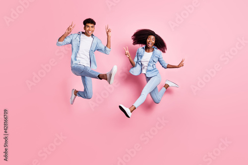 Full length body size view of beautiful handsome cheerful friends friendship jumping showing v-sign isolated on pink pastel color background