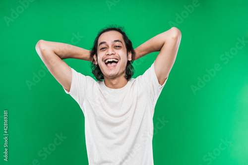 Portrait handsome man smiling happiness with long black hair while two hands behind the head isolated on green background