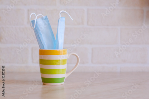 A yellow-striped teacup with medical masks into it sits on the kitchen table against a white brick wall.