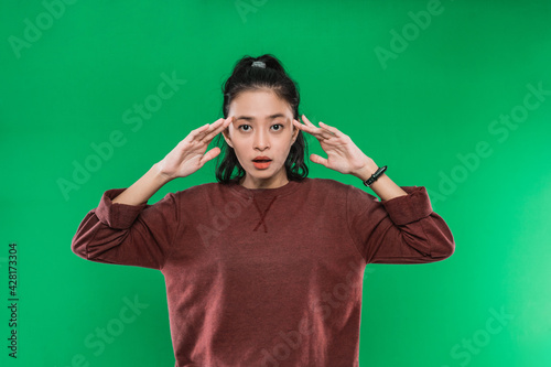 portrait young woman surprised expression raised her hand while holding his head and looked confused on green background