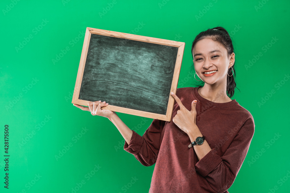 Young Asian woman presenting and pointing at something on a blank blackboard on a green background Young Asian woman presenting and pointing at something on a blank blackboard on a green background