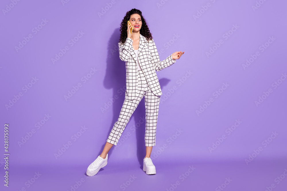 Full length body size portrait if woman talking on mobile phone looking blank space isolated on vivid purple color background Full length body size portrait if woman talking on mobile phone looking blank space isolated on vivid purple color background