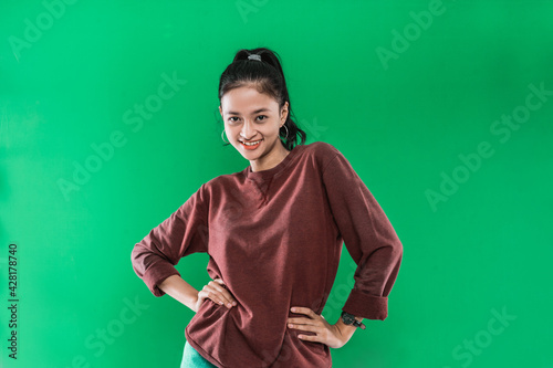 young Asian woman with hands at her hips while expression smiling off the face in green background