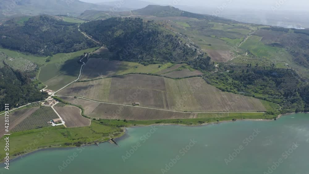 Lago Arancio in the heart of the Sicani mountains. The surrounding hills are planted with vineyards. Plows in action for the cultivation of vines. Wines of Sicily. Vineyards of Sicily. Spring.