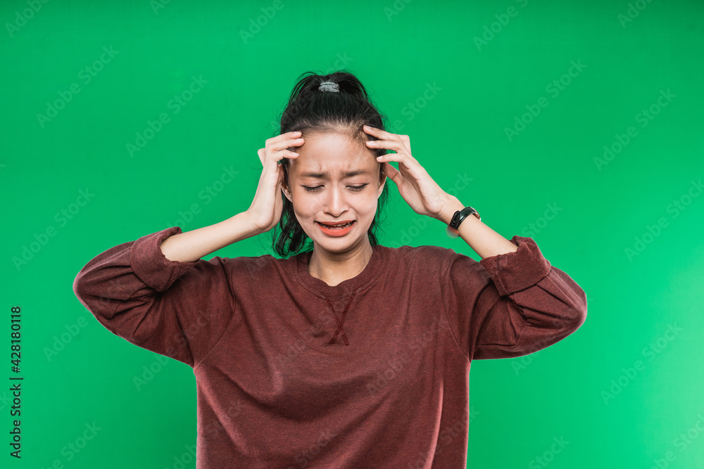 crying expression of a young Asian woman while holding the head with both hands a green background crying expression of a young Asian woman while holding the head with both hands a green background
