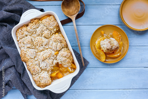 Foto Serving of freshly baked drop biscuit peach cobbler with apron and wooden spoon shot from top view