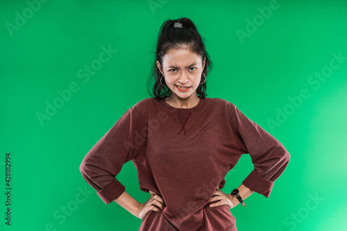 young Asian woman with hands at her hips while expression pissed off the face in green background
