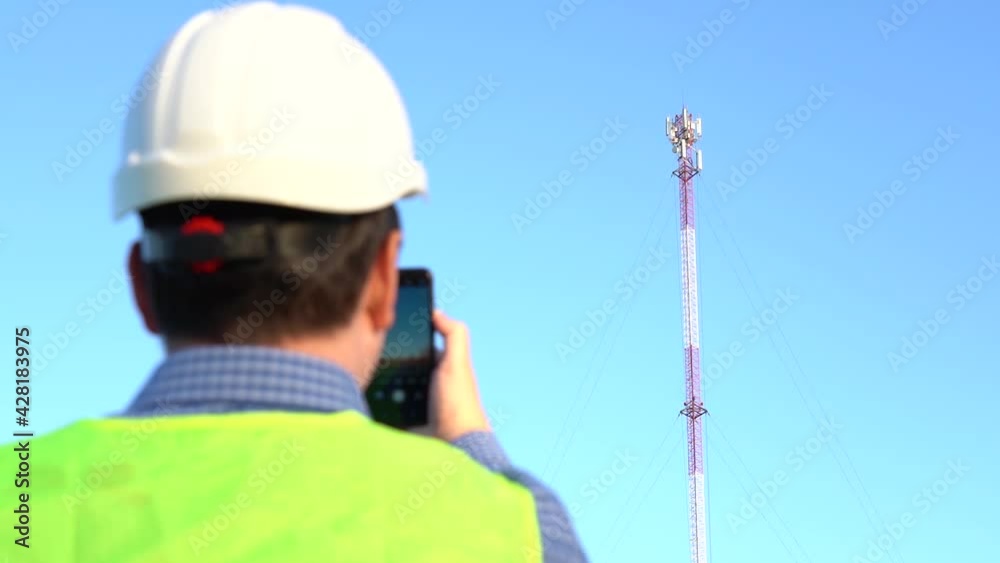 An engineer photographs a telecom tower for a report. Back view An engineer photographs a telecom tower for a report. Back view