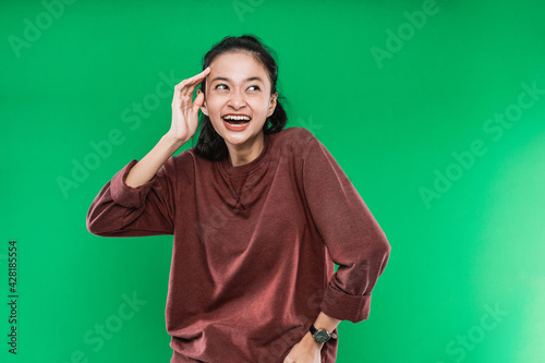 young Asian woman expressing happy wide-open mouth looking beside while one hand holding the head on green background