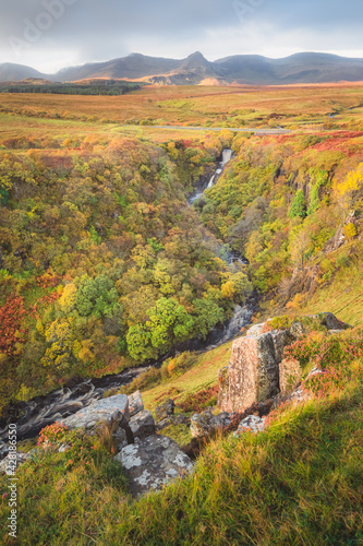 Scenic landscape view of Lealt Falls gorge ravine with vibrant  colourful Autumn foliage and mountain backdrop of Trotternish Ridge on the Isle of Skye  Scotland.