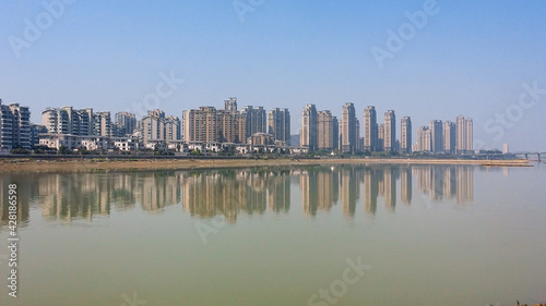 A panoramic view on the skyline of Fuzhou, China. The skyscrapers are reflecting in the Min River. The river has brownish color. Clear and blue sky. Modern, developed city.