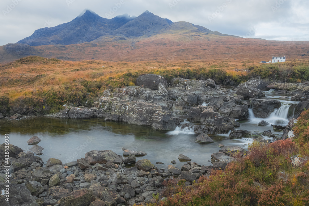 Fototapeta premium Scenic landscape view of the Black Cuillin mountains and a lone white croft house cottage at Sligachan waterfall on the Isle of Skye, Scottish Highlands, Scotland.