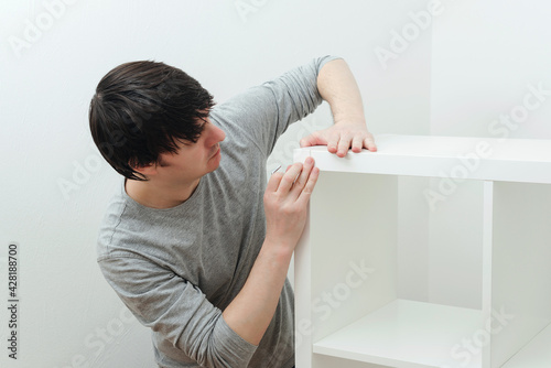 Man assembling new furniture at home. Furniture assembly yourself. Young worker collects a bookshelf.