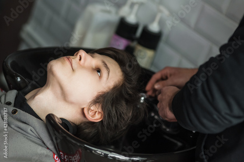 Close-up of brutal caucasian man having his hair washed in hairdressing salon. Barber washing head client. Barber at work