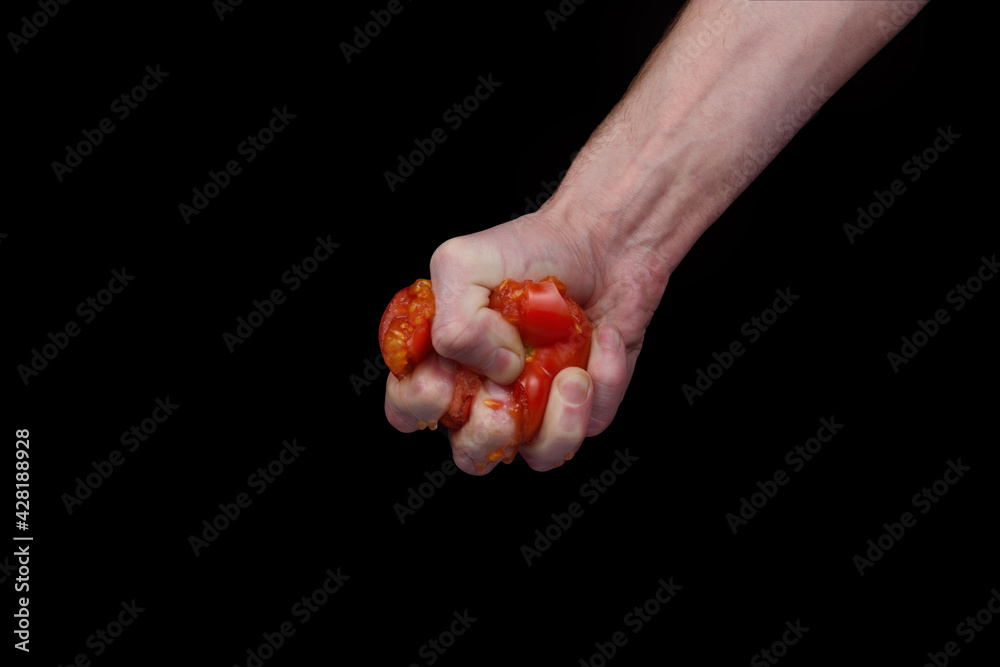 A man's hand crushes a red tomato on a black background. A man's hand crushes a red tomato on a black background.