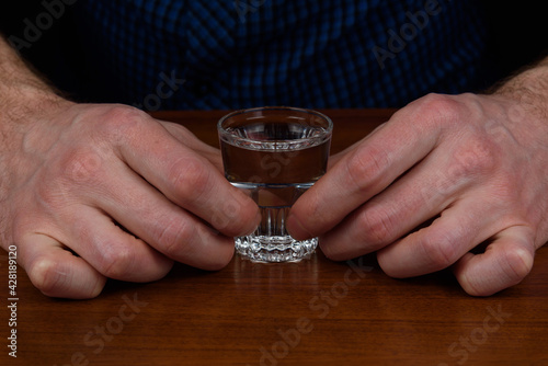 A shot with vodka is held by a man's hands.
