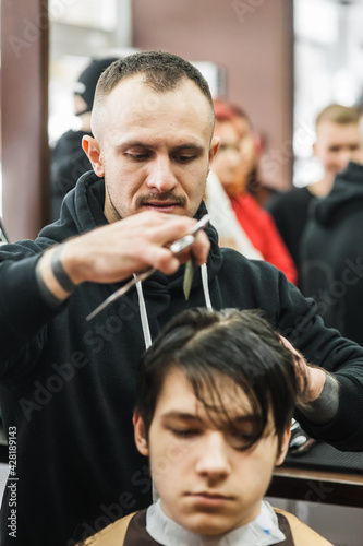 Hipster client man visiting in barber shop shaving hair. Modern guy having his hair cut in barbershop. © sharshonm