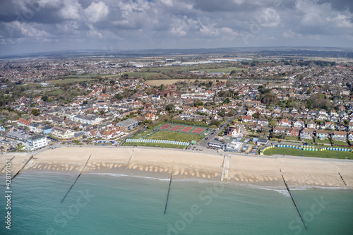 Felpham seafront in West Sussex with colourful beach huts on the coast and tennis courts in the background. Aerial View.