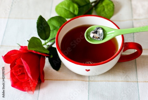 Tazza di te su una tovaglia a quadretti decorata con una rosa e un cucchiaio con un cuore di cristallo photo