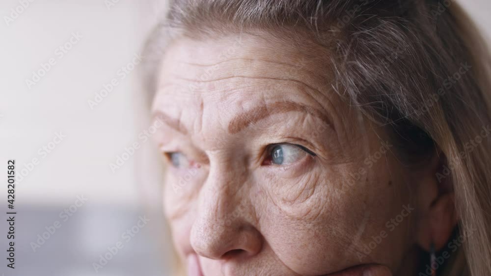 Sad elderly woman looking through the window. Depression and anxiety at old age. Close up. High quality 4k footage Sad elderly woman looking through the window. Depression and anxiety at old age. Close up. High quality 4k footage