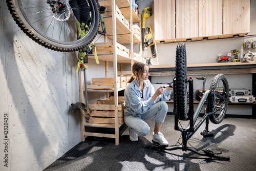 Young handywoman pumping bicycle wheels in the beautiful small workshop at home. Bicycle repairing and diy concept