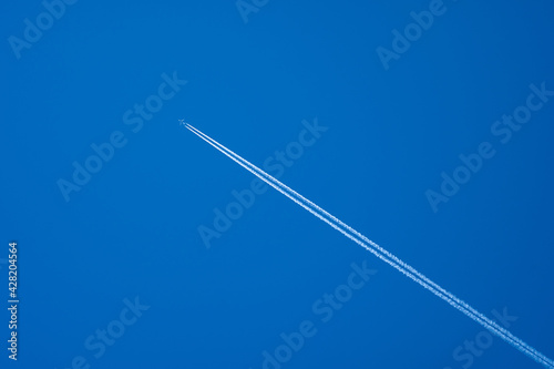 Airplane in flight with contrails in a clear blue sky
