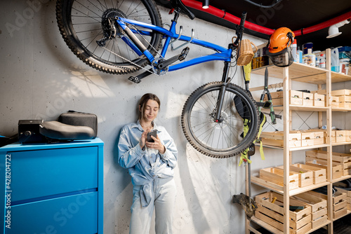 Portrait of a young handywoman standing relaxed with phone in the well equipped workshop or garage. DIY concept
