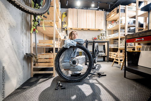 Portrait of a young handywoman reparing her bicycle in the beautiful small workshop at home. DIY concept