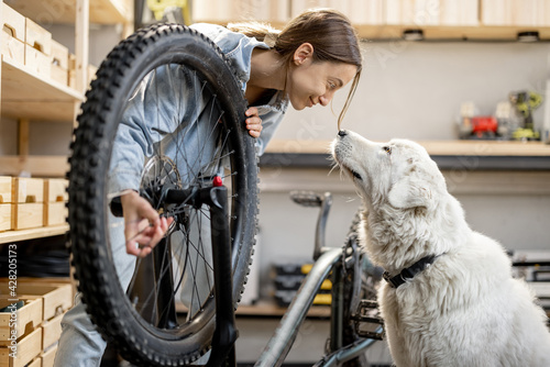 Young handywoman with her cute dog during a bicycle repairment in the home workshop or garage. DIY concept