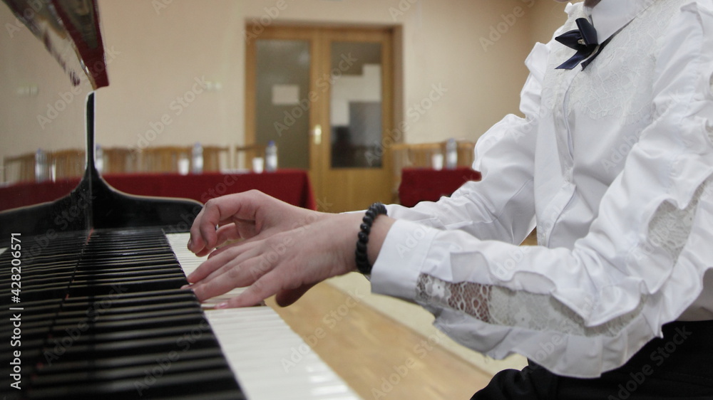 White hands of a young Caucasian piano girl playing the classical Grand piano against the background of an empty hall closeup, distance learning for music playing